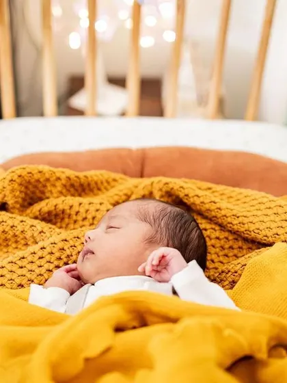 A newborn boy sleeping soundly in his own crib, wrapped in a cozy yellow blanket. These photos will be such a precious memory of his first room.