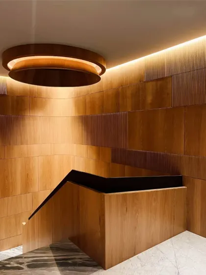 Another angle of the wooden staircase, showing how the light washes over the paneled walls. The descending staircase, enveloped in warm light, invites a harmonious transition between levels.
