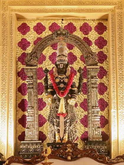 A direct view of the beautifully adorned deity, showcasing the craftsmanship of the silver-finished arch and the floral wall. Every detail is considered to honor the sacredness of the ceremony.