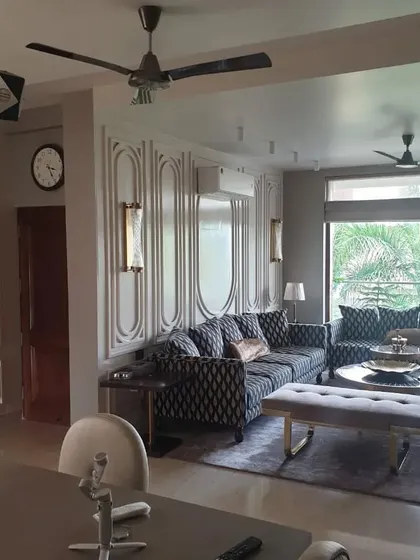 A luxurious living room with patterned sofas and elegant wall paneling. The design uses a sophisticated color palette and high-end finishes to create a formal and inviting space.