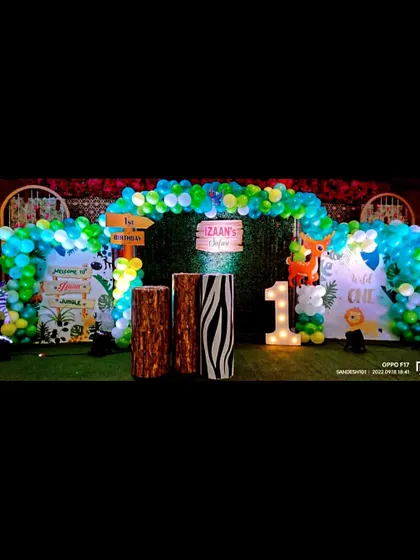 A "Wild One" jungle themed first birthday party. The outdoor setup on artificial grass includes a balloon arch, animal print pedestals, and a light-up number '1'.