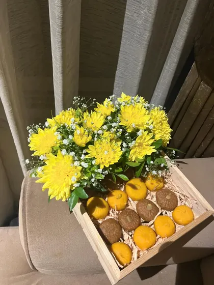 A wider view of the festive sweet tray, showing the simple, rustic charm of the wooden box paired with the vibrant yellow flowers and colorful sweets.