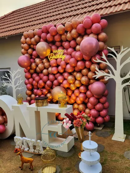 An outdoor first birthday with a full wall of rose gold balloons and large "ONE" letters.