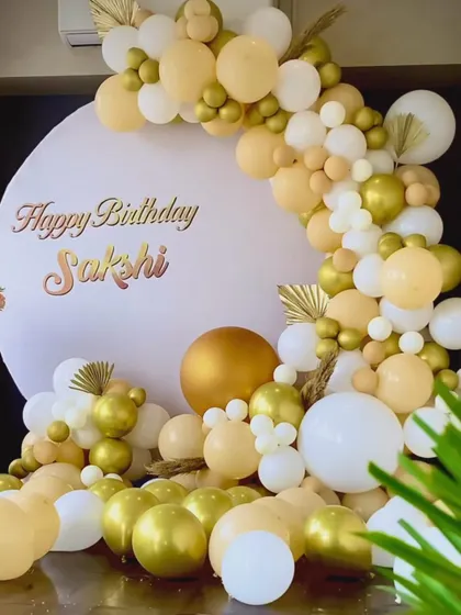 A beautiful birthday backdrop with a gold and white balloon arch. The use of dried palm leaves adds a touch of modern boho style.