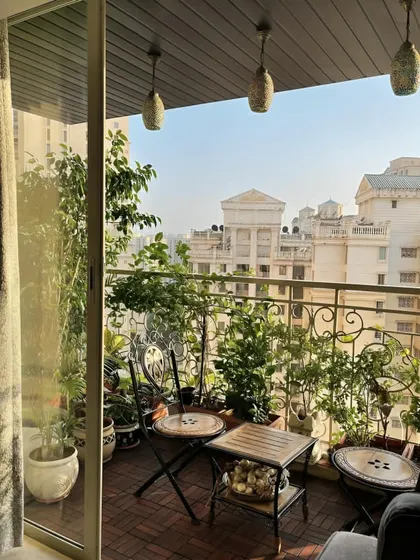 This classic Parisian-style balcony features a small mosaic bistro set, perfect for a coffee or a glass of wine. The space is filled with lush greenery, creating an intimate cafe feel with a city view.