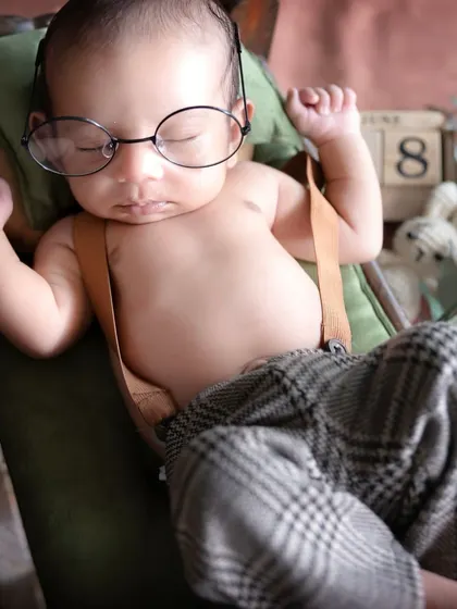 A close-up of our dapper little man, sleeping soundly with his tiny glasses. Every detail, from his suspenders to his relaxed hands, is just perfect.