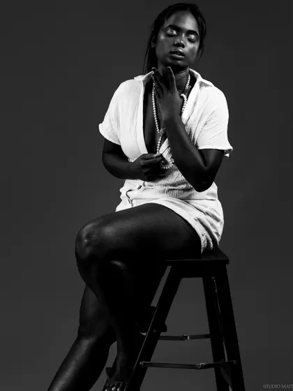 A powerful low-key black and white portrait of a model with dark skin, creating a beautiful contrast with her white outfit and pearl necklace. This is an example of my conceptual portrait work.
