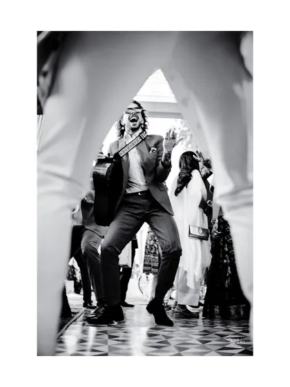 A black and white action shot of a band member, framed between the legs of another, capturing the dynamic energy of the musical performance.