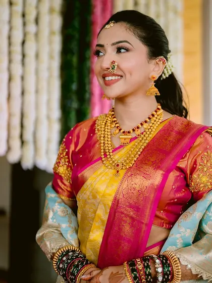A full view of this stunning Maharashtrian bride. The makeup is balanced to harmonize with the vibrant colors of her saree and the heavy gold jewelry, ensuring she looks elegant and feels comfortable.