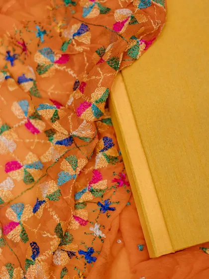 A detail shot of a yellow wedding album cover, resting on a beautifully embroidered orange fabric.