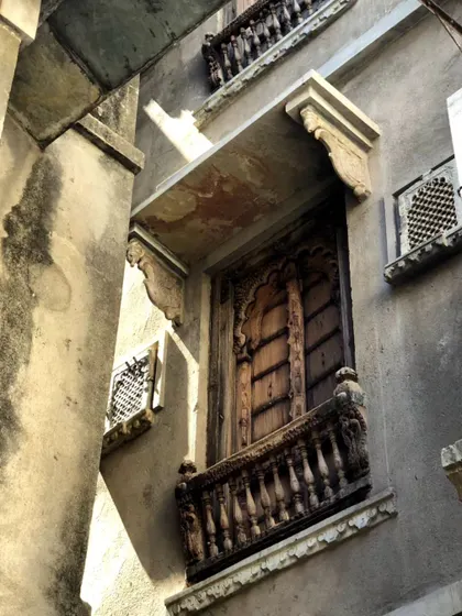 A weathered wooden balcony with detailed carvings, seen in Udaipur. The raw texture of the stone and the aged wood tell a story of time, influencing our use of honest and natural materials.