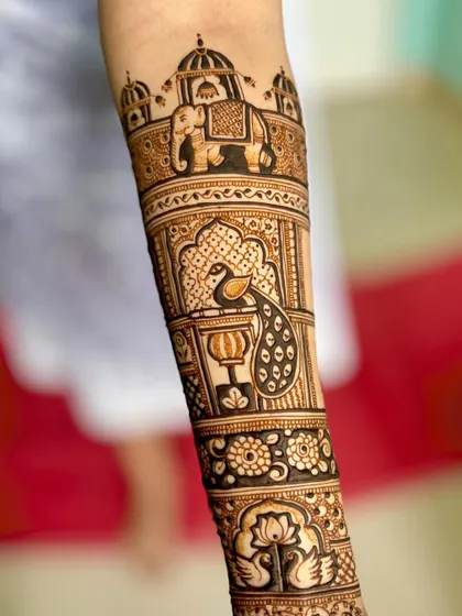 A close-up of the forearm, showcasing the majestic elephant and peacock motifs drawn with fine, precise lines.