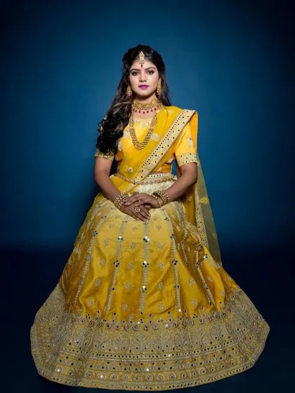 A seated portrait showcasing the beautiful drape and detail of the yellow traditional lehenga. The rich color and reflective mirror work ensure you stand out in every photo.