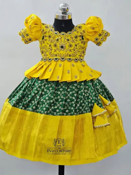 A bright yellow and green pattu pavadai with a peplum top. The yellow blouse has intricate embroidery, and the green skirt has a traditional yellow border.