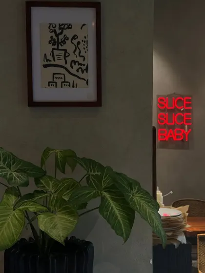 The interior of my restaurant combines modern art, lush greenery, and a playful neon sign. I wanted to create a vibe that is both stylish and comfortable, inviting you to stay a while.
