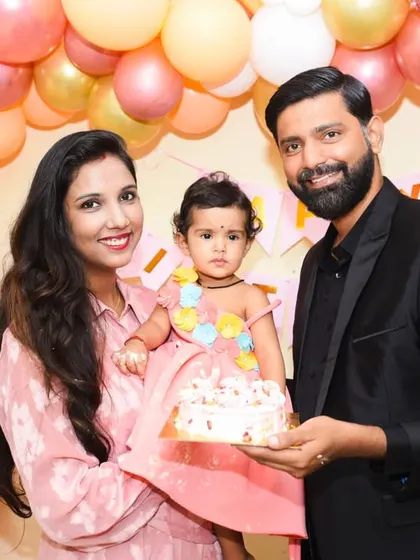 A classic family portrait with the birthday cake. The soft pink and gold balloon decor creates a warm and festive setting.