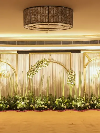 A full view of the elegant stage setup from the entrance. The symmetrical design with golden frames and floral arches creates a grand and picturesque focal point for the event.