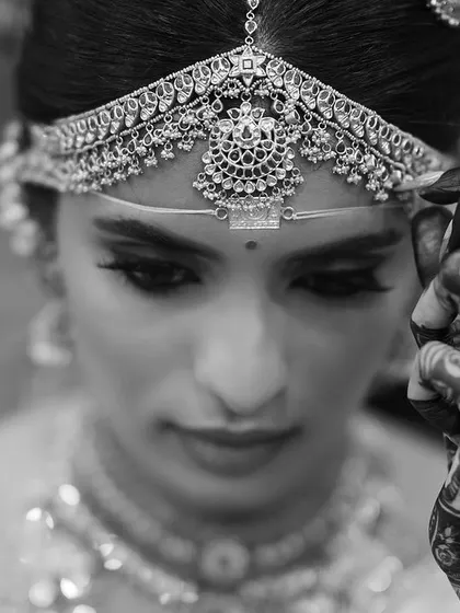 A stunning black and white portrait of the bride, her henna-adorned hand delicately touching her headpiece. This artistic shot is full of grace and emotion.