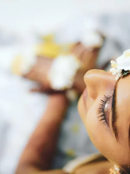 An artistic close-up shot from a haldi ceremony. The focus on the bride's eyelashes and floral maang tikka creates a delicate and beautiful image that captures the essence of the moment.