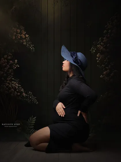 A creative and moody portrait. The mother-to-be, in a simple black dress and a stylish blue hat, is framed by floral elements in our studio.