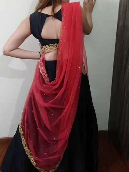 The back view of the black lehenga set, showing the stylish keyhole back of the blouse and the way the red net dupatta can be draped.