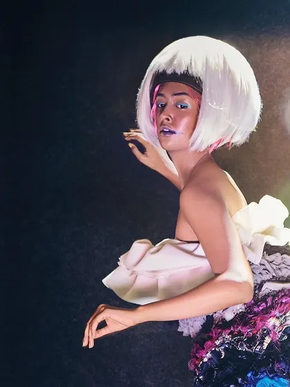 An avant-garde look combining a sculptural dress made from repurposed fabrics with a sharp, white bob wig. This styling choice creates a futuristic and artistic character for a high-concept editorial.