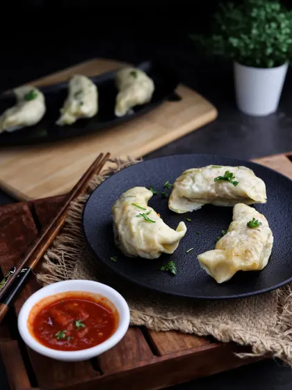Steamed momos served with a side of spicy sauce. The dark, rustic styling of this shot gives it an authentic, street-food feel that is very popular with audiences.