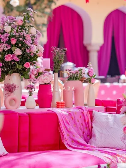 A cozy corner of the lounge, where a plush pink sofa is adorned with textured cushions and surrounded by an abundance of floral arrangements in modern vases.