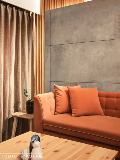 A closer view of the textural play in this living room, highlighting the soft velvet of the orange sofa against the raw finish of the concrete wall and the warmth of the vertical wood slats.