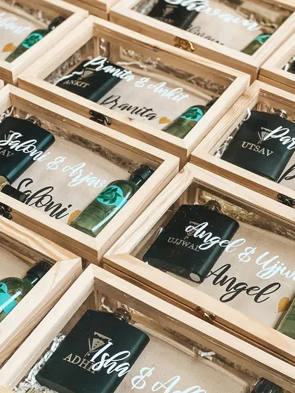 Personalized wedding favors in acrylic-lid wooden boxes, featuring custom-named hip flasks and miniature lotions for guests.