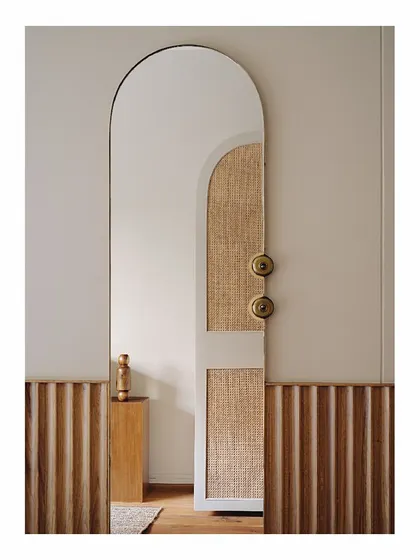 This arched mirror is integrated into a custom wardrobe design, which features natural cane panels. This piece combines storage, a full-length mirror, and beautiful materials into one seamless and elegant unit for the bedroom.