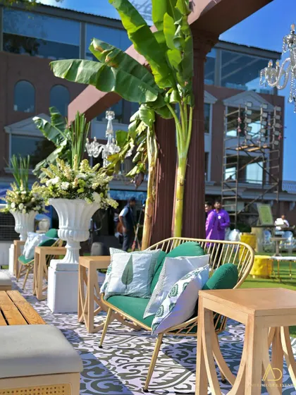 An exquisite seating arrangement featuring a green wicker sofa, printed cushions, and large banana plants, all set against a patterned floor.