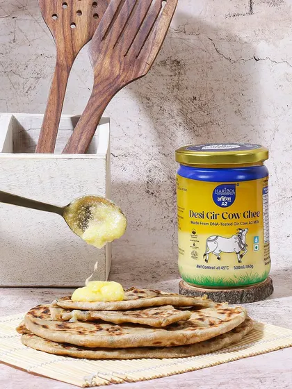 Here, the ghee is shown being added to hot parathas, a classic combination. This action oriented shot is highly relatable and effectively demonstrates a primary use case for the product in Indian kitchens.