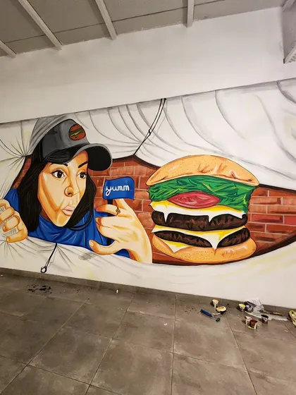 For the Novel Office cafeteria, we painted this fun 3D-effect mural of a woman peeking through a tear in the wall to admire a giant burger.