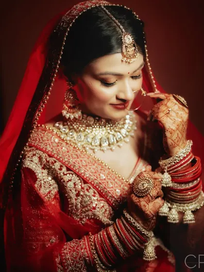 A detailed shot of the bride adjusting her bangles, highlighting the rich color of her lehenga and the intricate henna design.