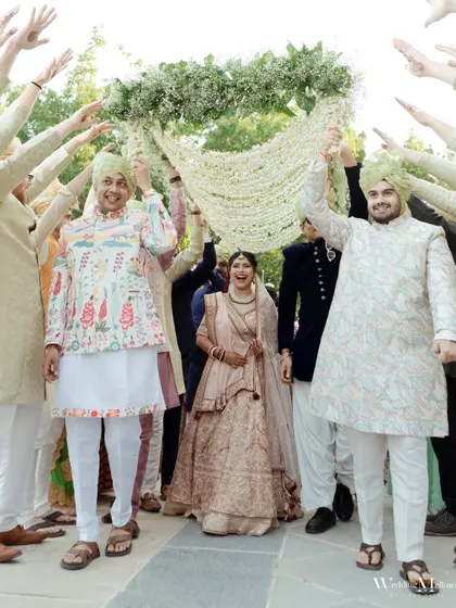 The bride makes her entrance under a 'phoolon ki chadar' held by her brothers and friends. This photo captures the joy and support of family during this significant moment.