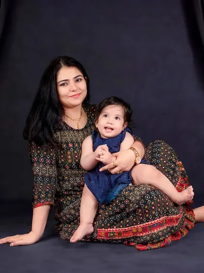 A mother and her baby share a happy moment, seated against a classic dark backdrop. The baby's joyful expression is the highlight of this portrait.