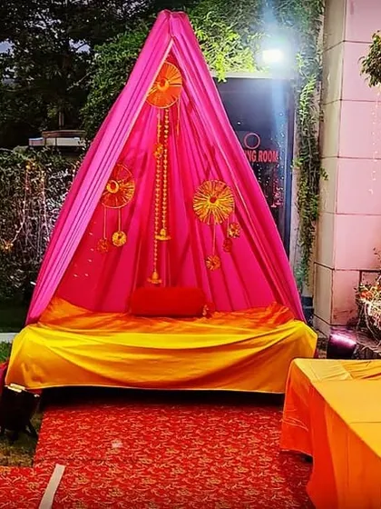 A simple and traditional canopy setup for an intimate home ceremony. The bright pink tent is decorated with marigold garlands and provides a sacred space for wedding rituals.