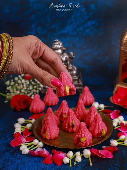 Rose-flavoured modaks, styled with fresh rose petals and jasmine flowers. The human touch, with bangles and henna, adds a beautiful cultural and personal element.