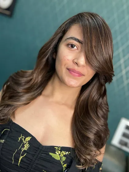 A beautiful client showcasing her new elegant brown hair with face-framing layers and soft waves.