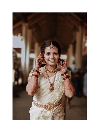 A happy bride adjusts her jewellery in a temple corridor.
