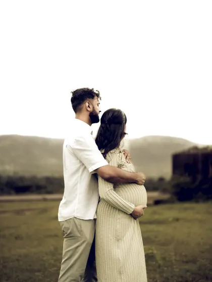 The couple stands together, looking out at the horizon. His arm around her is a gesture of protection and unity as they contemplate their future family.