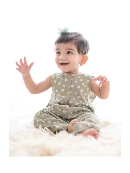 A happy baby girl in a cute green romper, waving at the camera during her studio session.