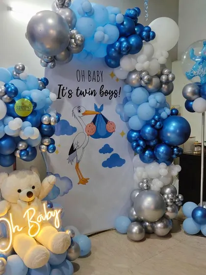 Double the joy! A grand "Oh Baby, It's twin boys!" welcome home decoration. The blue and silver balloon setup with a stork graphic and a neon sign makes for a big celebration.