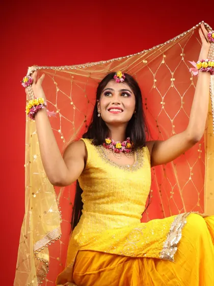 The bride-to-be looking radiant under her golden dupatta. The colorful eye makeup adds a playful touch to the traditional Haldi look.