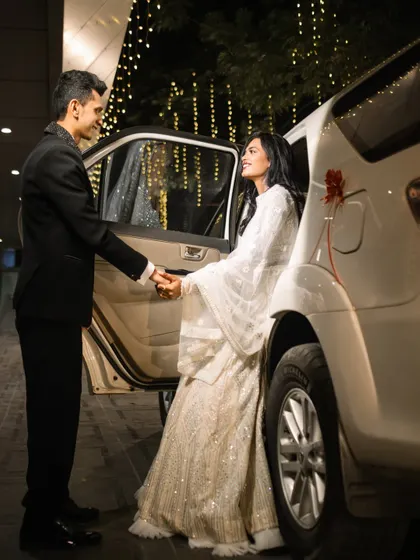The groom helps his bride out of the car, a classic, chivalrous moment captured beautifully. The background fairy lights add a touch of magic to this stylish and candid reception photo.