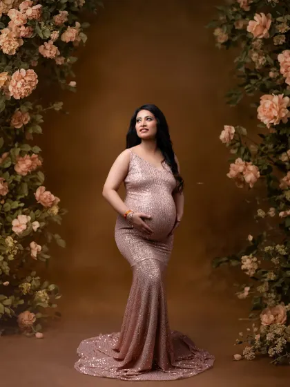 A glamorous solo portrait of the mother-to-be in a sparkling rose gold sequin gown, framed by a beautiful floral arch.
