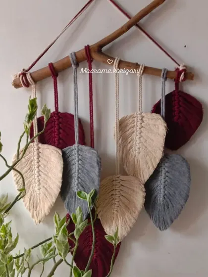 A macramé wall hanging featuring feathery leaves in maroon, grey, and beige. This piece brings a touch of nature-inspired art to your walls.