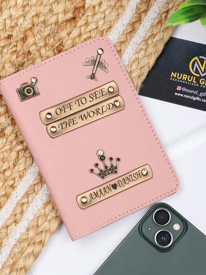 A beautiful pink passport cover, fully customized with two names, multiple charms like a camera and airplane, and the inspiring quote 'Off to see the world'.