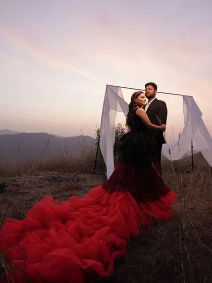 A stunning pre-wedding portrait at dusk. The couple stands before a simple white frame, letting the dramatic gown and the evening sky take center stage.